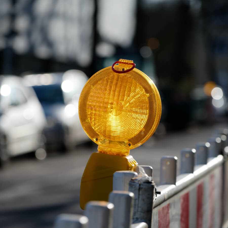 Flashing yellow construction light mounted on road barrier in daylight